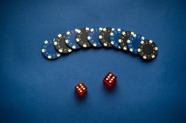 Siyah ve mavi oyun çiplerinden oluşan bir koleksiyon, iki kırmızı zarın yanında iki numara altıları gösteren bir eğri şeklinde düzenlenir. Oyun gecesi için ortam rahat ve ideal..