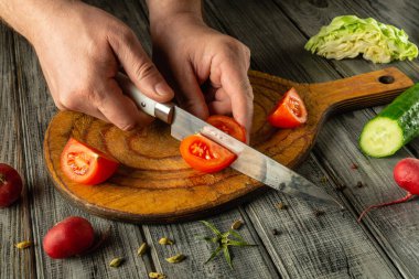 Taze sebzelerle çevrili ahşap bir tahtanın üzerinde ustalıkla kesilmiş domatesler, canlı, doğal malzemelerle pişirme sanatını sergiliyor..