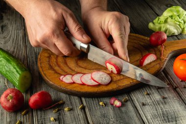 Salatalık ve marul da dahil olmak üzere bir dizi taze sebze ile çevrili, rustik ahşap kesme tahtasının üzerinde ustaca kesilmiş turplar. Güneş ışığı çalışma alanını aydınlatır.