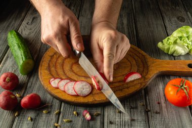 Eller ahşap bir tahtanın üzerinde turpları ustalıkla dilimler. Mutfak ortamında salatalık, domates ve marul gibi taze sebzelerle çevrili..