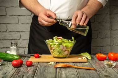 Bir şef marul, turp ve salatalıkları bir kaseye karıştırarak ve iyi donanımlı bir mutfakta zeytinyağı sosu ekleyerek taze bir salata hazırlar..