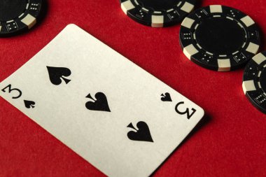 Oyuncuların bir sonraki hamlelerini düşündükleri bir poker oyunu başladı. Siyah ve beyaz çiplerle çevrili kırmızı bir masanın üzerinde duran maça üçlüsü rekabetçi bir atmosfer sergiliyor..