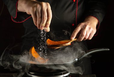 Bir şef, buharla çevrili tatlı patates dilimlerinin üzerine baharat serpiyor. Mutfak hazırlıklarının beceri ve konsantrasyonunu yakaladığımız an.