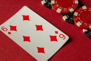 Siyah ve kırmızı poker çiplerinin yanında karo altılısını gösteren bir oyun kartı. Oyuncular hareketli bir oyuna girerken masa canlı kırmızı bir keçeyle kaplıdır..