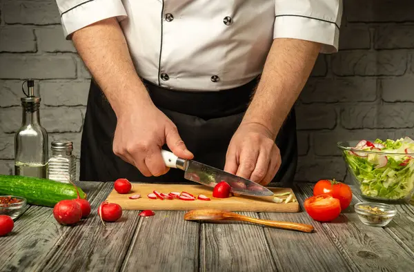 Bir şef ustalıkla ağaç kesme tahtasında sebze doğruyor. Sıcak bir mutfak atmosferinde taze domates, turp ve salatalık mevcuttur..
