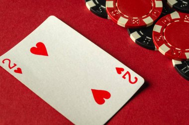 Kupa kartlarından ikisi kırmızı bir masanın üzerinde duruyor. Etrafı renkli poker fişleri ile çevrili. Arkadaşlarla heyecanlı bir oyun gecesi için hazırlar..
