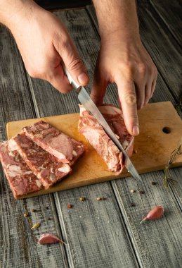 Kırsal ahşap bir kesme tahtasında bir insan taze et dilimliyor. Etin etrafında sarımsak karanfilleri ve taze otlar var. Sıcak bir aşçılık atmosferi yaratıyorlar..