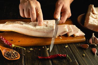 Sarımsak ve kırmızı biber gibi canlı baharatlarla çevrili ahşap bir tahtanın üzerinde ustalıkla kesilmiş et. Kaba bir mutfak ortamı mutfak deneyimini geliştirir..