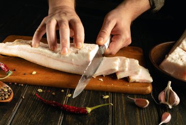 Eller ustalıkla büyük bir parça domuz yağını baharatlarla süslenmiş ahşap bir kesme tahtasına dilimler. Sıcak ortam yemek hazırlama sırasında aşçılık deneyimini arttırır..