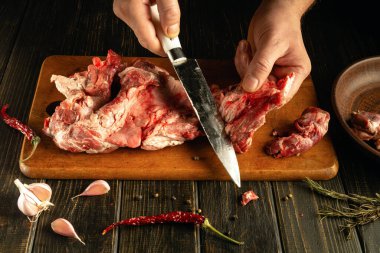 Sarımsak, kurutulmuş kırmızı biber ve karabiber ile çevrili ahşap bir tahtanın üzerinde ustalıkla çiğ et kesen bir insan köylü mutfağında yemek hazırlıyor..