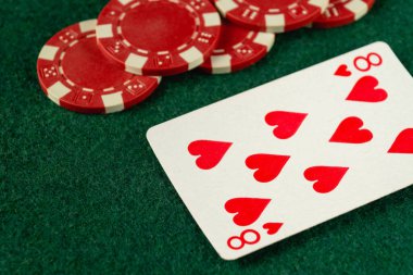İçinde kalpler ve kırmızı poker fişleri olan iskambil kartları yeşil bir keçeli masa üzerinde düzenlenir. Ayarlar, aile veya arkadaşlar arasında canlı bir kart oyunu gecesi olduğunu gösteriyor..