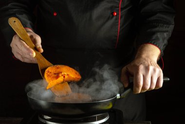 Becerikli bir aşçı fırında tavada canlı bir portakal karışımı pişirir. Etrafı kıvrımlı buharla çevrili, profesyonel bir mutfak ortamında mutfak uzmanlığı sergiliyor..