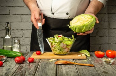 Mutfakta, bir şef taze salata hazırlarken lahana ve turpları ustalıkla doğruyor. Taze domates ve salatalıklar kesme tahtasının etrafını sararak canlı görüntüyü güçlendirir..