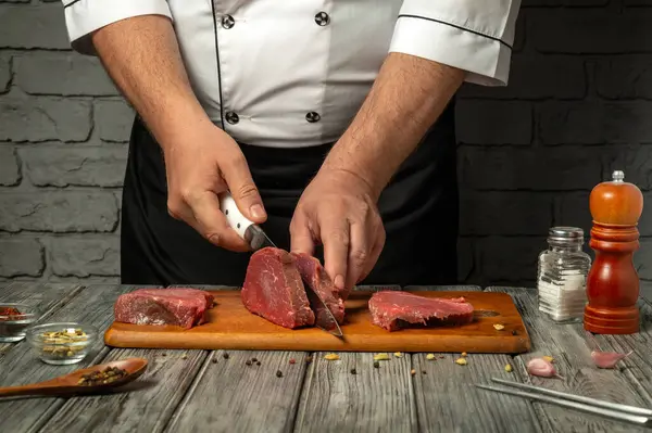 Yetenekli bir şef sıcak bir mutfakta tahta bir tahtada taze et kesiyor. Mutfak hazırlıklarını vurgulayarak, çeşitli baharatlar, baharatlar ve mutfak aletleri sahnenin çevresini sardı.