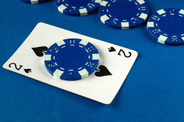 Maça kartlarından ikisi mavi bir poker çipinin tepesinde, mavi bir yüzey üzerinde daha fazla fiş ile çevrili, arkadaşlarıyla kağıt oynadığı neşeli bir gecenin özünü yakalıyor..