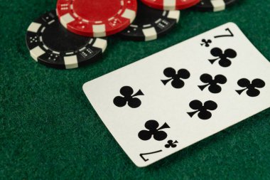 Canlı bir oyun oturumu sırasında canlı yeşil keçeli yüzeye kurulmuş çeşitli poker çiplerinin yanında sinek yedilisini gösteren bir oyun kartının yakın plan görüntüsü..