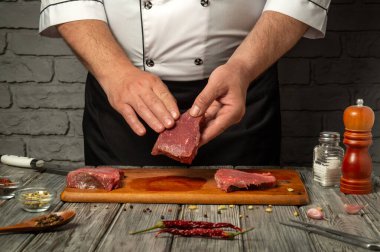 Şef, baharatlar, otlar ve kırsal mutfak zeminiyle çevrili ahşap bir kesme tahtasının üzerinde ustalıkla taze et dilimleri hazırlıyor..
