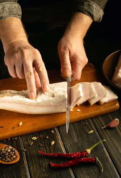 Taze domuz yağı dikkatlice ahşap bir kesme tahtasıyla kesilir. Eller ustalıkla bir bıçak kullanır, çeşitli rengarenk baharatlarla çevrili, canlı bir yemek atmosferi yaratır..