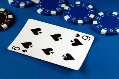Maça dokuzlu bir kart çeşitli mavi ve siyah poker çiplerinin yanında belirgin bir şekilde sergilenmektedir, bu da arkadaşlarla akşam buluşmalarında tipik bir evde oynanan canlı poker oyununa işaret eder..