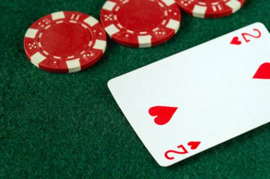 Yeşil keçeli masaya dağılmış bir kalp ve birkaç kırmızı poker fişi gösteren bir iskambil kağıdının yakın çekimi. Atmosfer canlı ve dostça bir rekabet için davet edici..