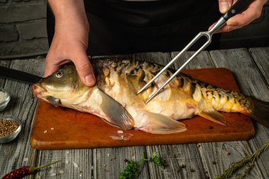 Eller ustalıkla ahşap bir kesim tahtasının üzerinde taze bir balık hazırlıyor, kırsal bir mutfak ortamında otlar ve baharatlarla çevrili, davetkar bir mutfak atmosferi yaratıyor..
