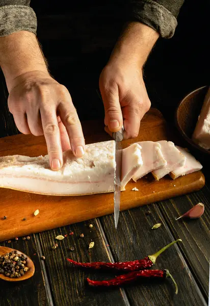 Bir şef, ahşap kesme tahtasındaki taze balıkları ustalıkla dilimlerken dikkatle odaklanır. Yakınlarda çeşitli baharatlar ve kırmızı biberler var. Mutfak atmosferini geliştiriyorlar..