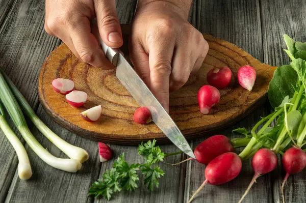 Elleri ahşap bir tahtanın üzerinde canlı turpları ustalıkla dilimler, taze sebzeler ve otlarla çevrili, sıcak bir mutfak atmosferinde sağlıklı pişirmenin özünü yakalar..
