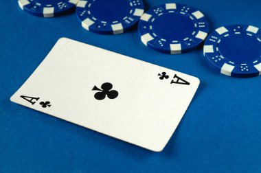 Yakın çekimde, bir kulüp kartının yakınlarda birkaç mavi poker fişi bulunan bir yüzeye yerleştirildiği görülüyor. Kurulum oyun ya da kumarhane ortamını gösteriyor..