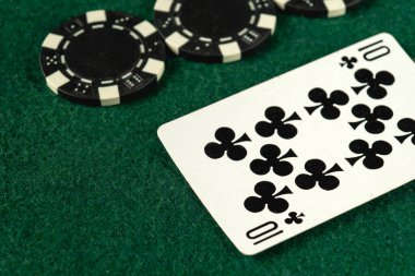 Yeşil keçeli bir yüzey üzerinde on numara sinek ve birkaç siyah poker çipini gösteren bir oyun kartının yakın çekimi. Bu ayar, gece devam eden bir poker oyununu gösterir.
