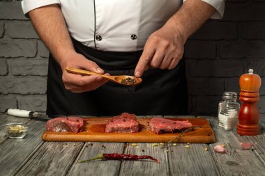 Bir şef, kaşıktan baharat serperek çiğ et hazırlar. Yemek pişirme becerilerini sergiler. Mutfak iyi aydınlatılmış, taze malzemelere odaklanmamızı sağlıyor..