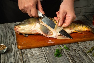 Bir aşçı ustalıkla fileto yapar. Sıcak bir mutfakta ahşap bir kesme tahtasının üzerinde taze bir balık. Eller keskin bir bıçak kullanarak detaylara dikkat eder. Taze bitkiler ve baharatlar yakına renk katar..