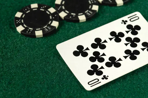 Yeşil keçeli bir yüzey üzerinde on numara sinek ve birkaç siyah poker çipini gösteren bir oyun kartının yakın çekimi. Bu ayar, gece devam eden bir poker oyununu gösterir.