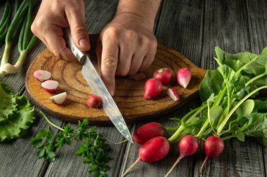 Eller dikkatlice taze yeşillik ve otlarla çevrili ahşap bir tahtanın üzerinde gevrek turpları dilimliyor, canlı bir ev yemeği aktivitesi sergiliyor..