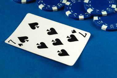 Mavi poker fişleri ile çevrili canlı mavi bir yüzey üzerinde maça yedili bir kart düz yatar, devam eden bir kart oyunu ve yarışmanın heyecanını gösterir.