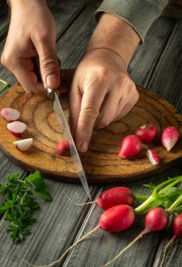 Taze otlarla çevrili yuvarlak bir ahşap kesme tahtasının üzerinde parlak kırmızı turpları ustaca dilimle. Sıcak ışık mutfağın rahat atmosferini vurgular..
