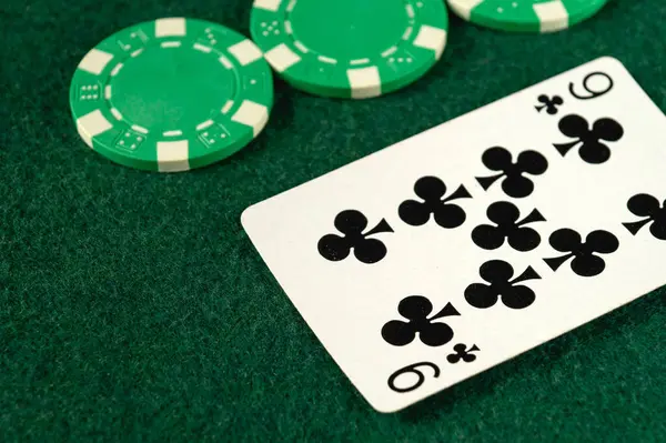 Parlak yeşil poker fişleri ve sinek dokuzlunun yeşil keçeli bir yüzey üzerinde yattığını gösteren bir kart, geceleri arkadaşlar arasında neşeli bir kart oyunu için ortam hazırlıyor..