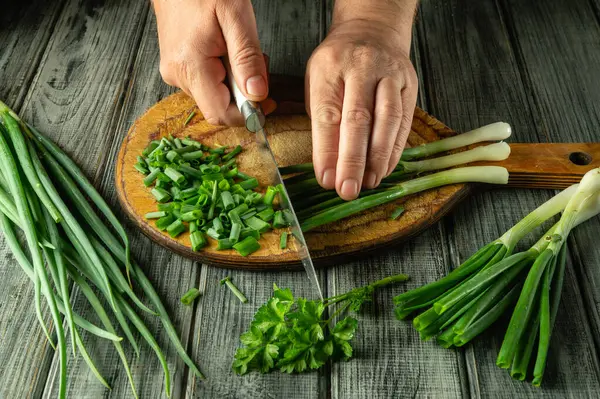 Taze yeşil soğanlar ustalıkla tahta kesme tahtasında doğranıyor. Doğal ışık, sebzelerin canlı renklerini güçlendirir ve davetkar bir mutfak atmosferi yaratır..