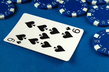 Maça altılısını gösteren bir kart, çeşitli mavi poker fişleri ile çevrili, mavi bir keçeli arka planda yatar..