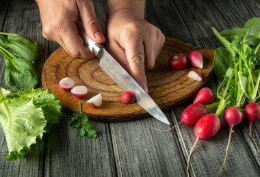 Turpları ve yapraklı yeşillikleri taze ürünlerle çevrili ahşap bir tahtanın üzerinde ustalıkla dilimlemek. Canlı renkler ve doğal ışık bileşenlerin tazeliğini vurgular..