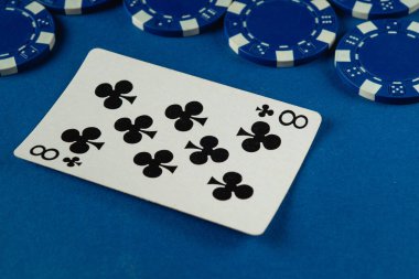 Sinek sekizli bir kartın yakın plan görüntüsü canlı mavi bir masada, birkaç mavi poker çipinin yanında duruyor..
