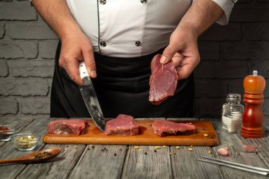 Yetenekli bir şef profesyonel bir mutfakta tahta bir tahtada taze et dilimler. Çeşitli baharatlar ve kaplar düzgünce düzenlenir, mutfak hazırlıkları sergilenir.