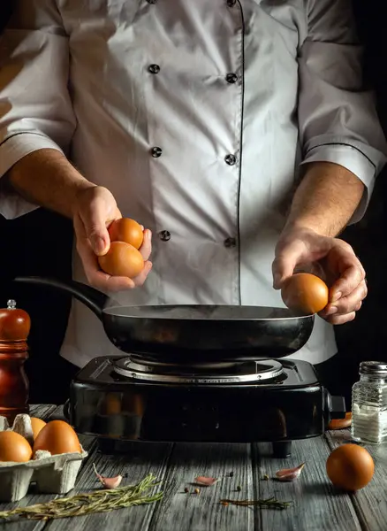 Sıcak, davetkar bir mutfakta, bir şef taze yumurta kırmaya hazır bir tavanın başında durur. Sahne, sabah pişirme rutininin özünü yakındaki malzemelerle yakalıyor..