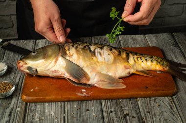 Bir insan taze yakalanmış bir balığı tutarken, kişniş pişirirken üzerine de kişniş koyar. Ayarda, yakınlarda çeşitli baharatları olan kırsal ahşap bir tezgah yer alıyor..