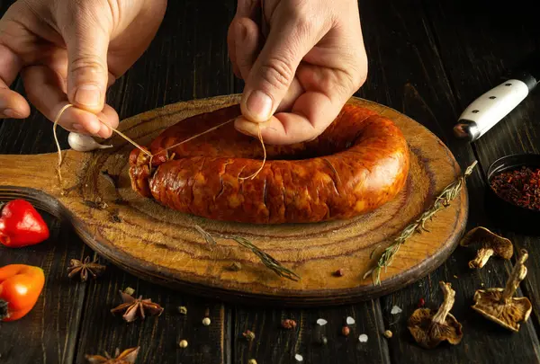 Yetenekli eller, rengarenk baharatlar ve taze malzemelerle çevrili ahşap bir tahtaya baharatlı bir sosis bağlar. Hazırlık aşamasında aşçılık sanatını sergilerler..