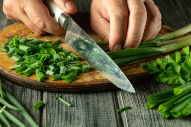Kırsal kesim tahtasında yeşil soğanları ustalıkla doğrayan bir insan, taze kesilmiş otlarla çevrili, doğal ışıkla dolu, davetkar bir mutfakta..