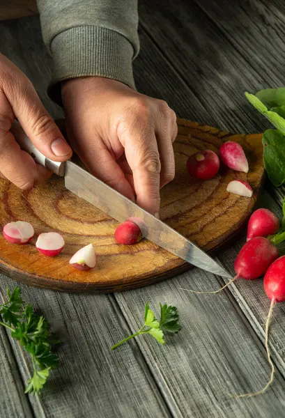 Ahşap bir kesme tahtasındaki kırmızı turpları ustalıkla dilimle dilimle. Yakınlarda taze bitkiler var. Sıcak bir mutfakta canlı bir yemek atmosferi yaratıyorlar..