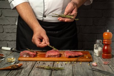 Köy mutfağında, bir şef çiğ eti taze otlarla, mutfak tekniklerini ve kaliteli malzemelerin kullanımını dikkatlice mevsimlendirir. Atmosfer aşçılığa olan bağlılığı yansıtıyor..