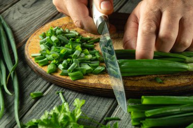 Taze otlarla çevrili ahşap kesme tahtasındaki yeşil soğanları ustaca dilimle. Mutfak ortamında kırsal bir hava var. Mutfak aktivitelerini arttırıyor..