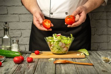 Bir şef salata hazırlarken sıcak bir mutfakta durur. Salatayla dolu temiz bir kaseye taze domates ve turplar ekleniyor. Mutfak aletleri ve malzemeleri yakında..