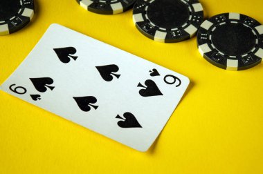 Maça dokuzlu bir kart sarı bir yüzeye uzanır. Birkaç siyah beyaz poker çipinin yanında. Bu da heyecanlı bir oyun gecesi atmosferini gösterir. Çelişkili renkler görsel cazibeyi arttırır.